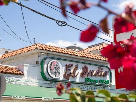 El Indio Mexican Restaurant storefront on India Street with its neon 'El Indio Since 1940' sign, red-tile roof and green awning, framed by bougainvillea